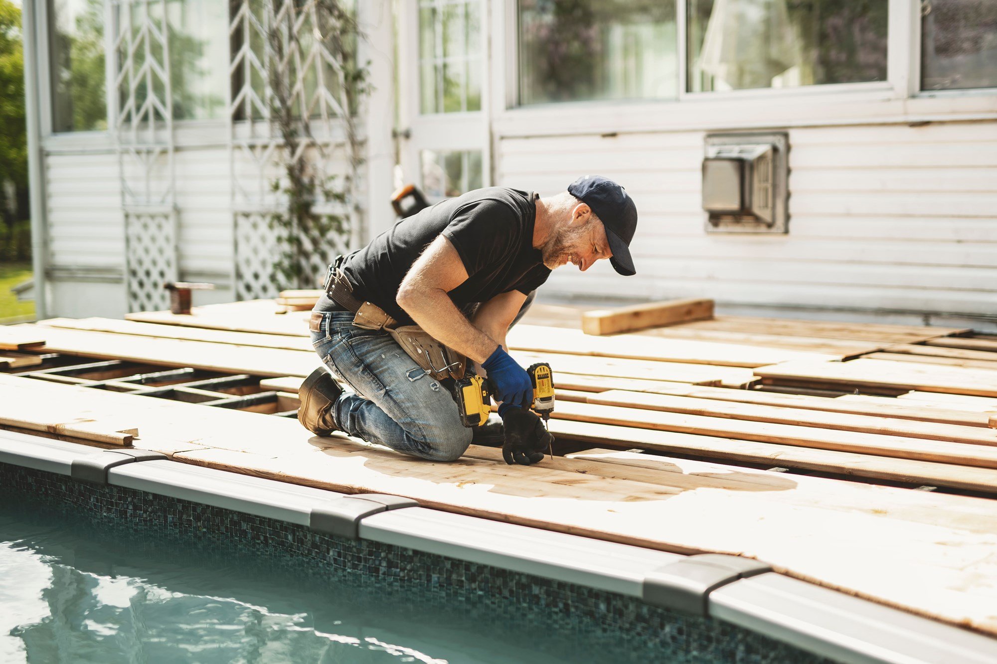Homme en train d’installer une terrasse en bois autour d’une piscine hors terre avec une perceuse-visseuse