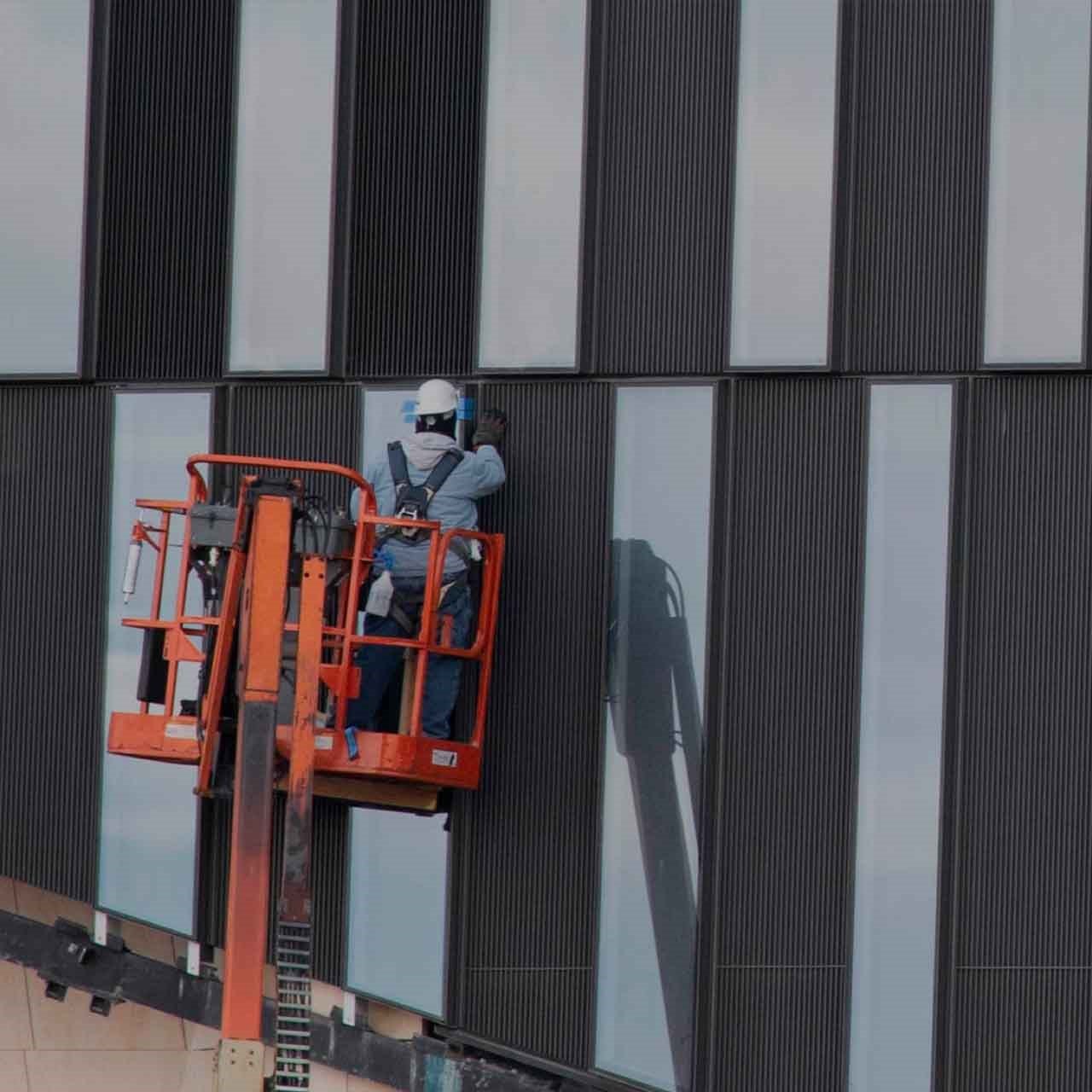 Un ouvrier dans une nacelle louée chez Simplex face à un mur noir et blanc qui est entrain de travailler sur un chantier en hauteur.