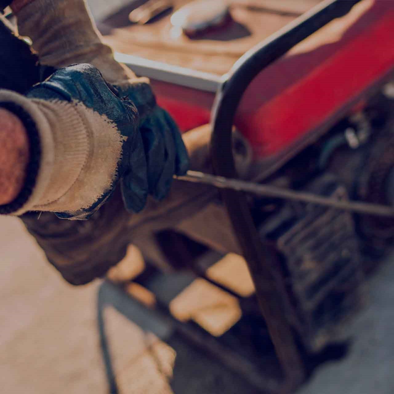 Mains d'un ouvrier en gants de chantier tirant sur le câble de démarrage pour mettre en marche une génératrice sur le chantier.