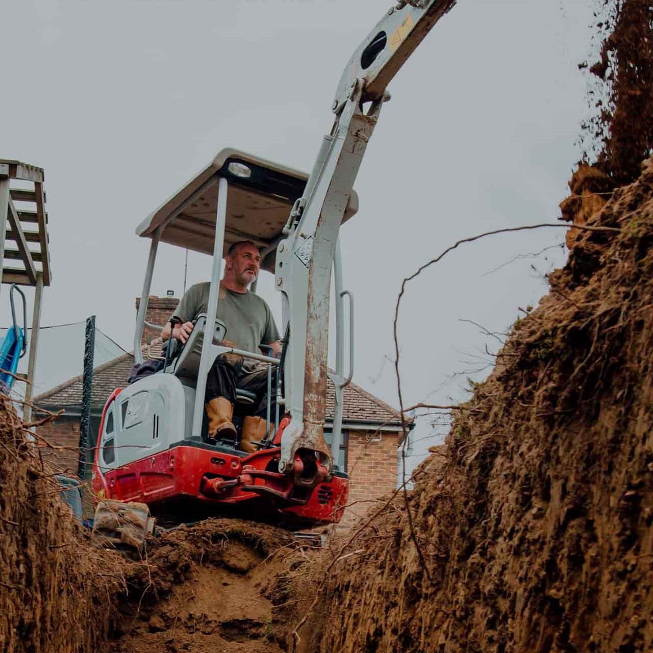 Homme manœuvrant une mini excavatrice blanche et rouge en location pour creuser un trou dans la terre.